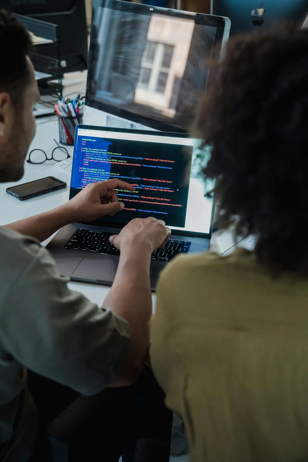 GP ORGAPLAN – Organisationsplanung und Strukturlösungen – Das Bild zeigt einen Moment professioneller Zusammenarbeit, wahrscheinlich eine Pair-Programming-Session, bei der zwei Personen Code auf einem Laptop-Bildschirm analysieren, um ein Problem zu lösen oder die Arbeit zu überprüfen.